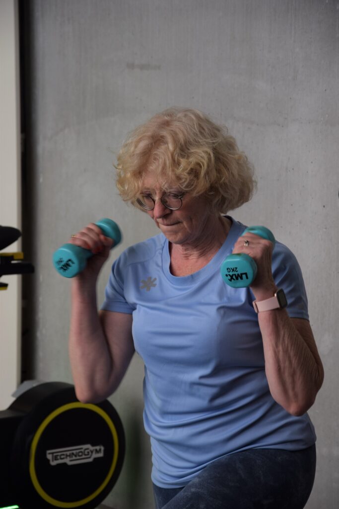 Vrouw van vijftig-plus traint met dumbbells om haar spiermassa te behouden