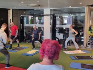 Deelnemers aan een groepsles doen lunges op de mat, waarbij ademhaling het tempo bepaalt