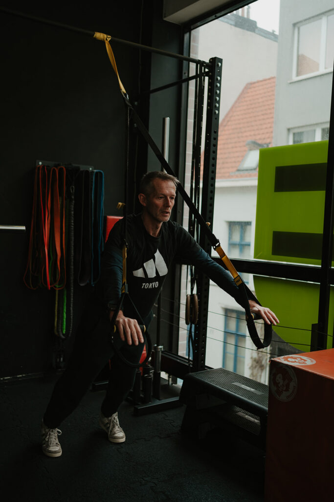 Man van midden veertig traint met TRX-banden na een werkdag aan het bureau