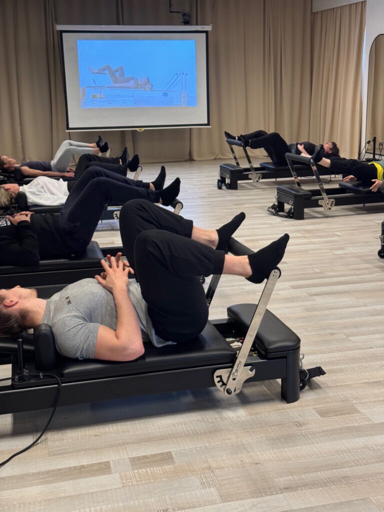 Deelnemers trainen benen en core op de Reformer met gebogen knieën tegen de veerweerstand