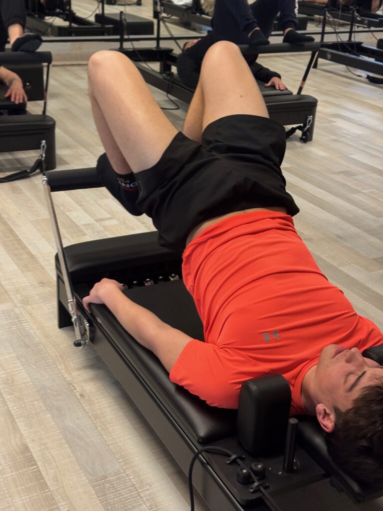 Deelnemer traint liggend de diepe buikspieren op de Reformer met de benen in tafelpositie
