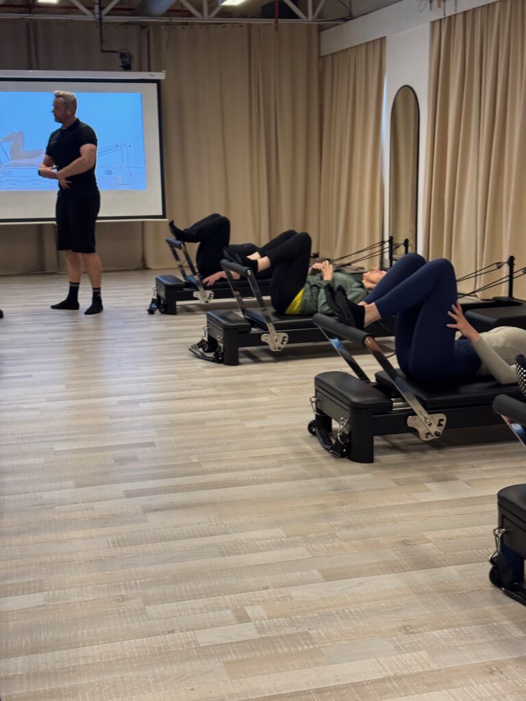 Coach geeft uitleg aan de groep bij het scherm tijdens een Reformer Pilates les bij Fitality