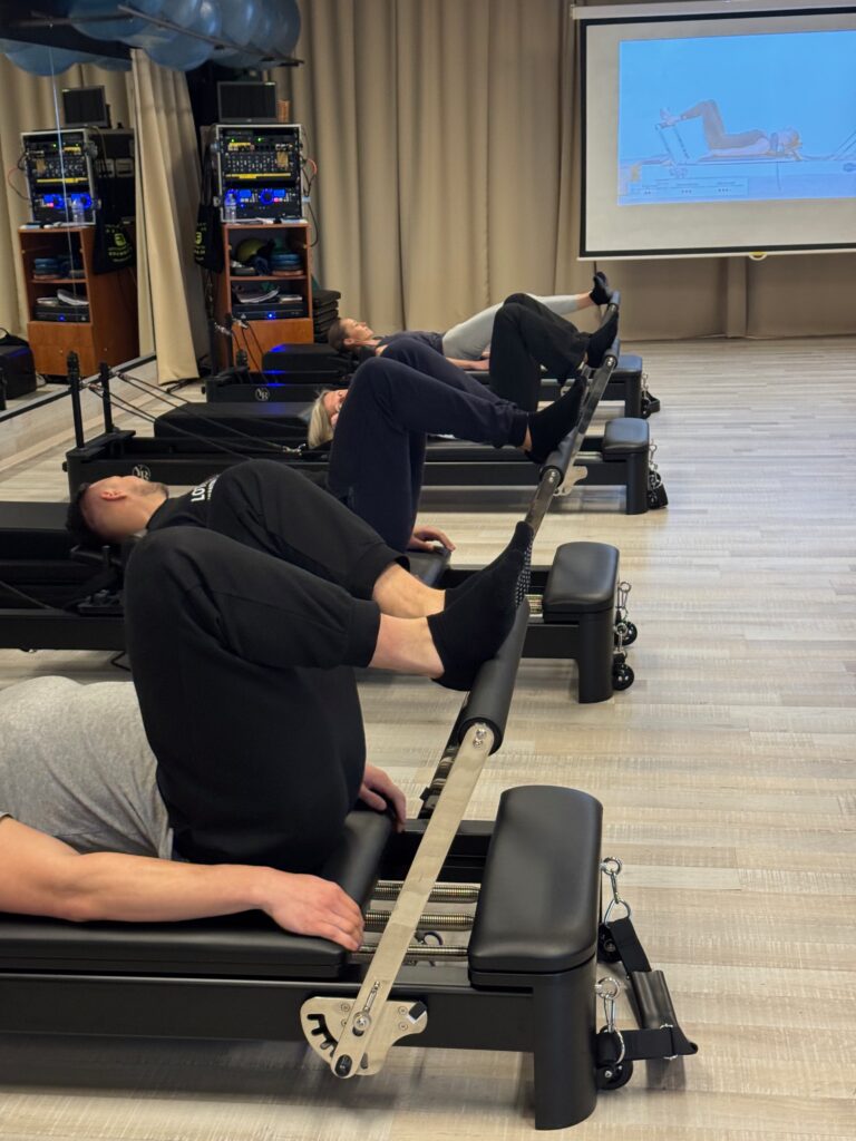 Deelnemers voeren liggend een footwork-oefening uit op de Reformer tijdens een groepsles bij Fitality