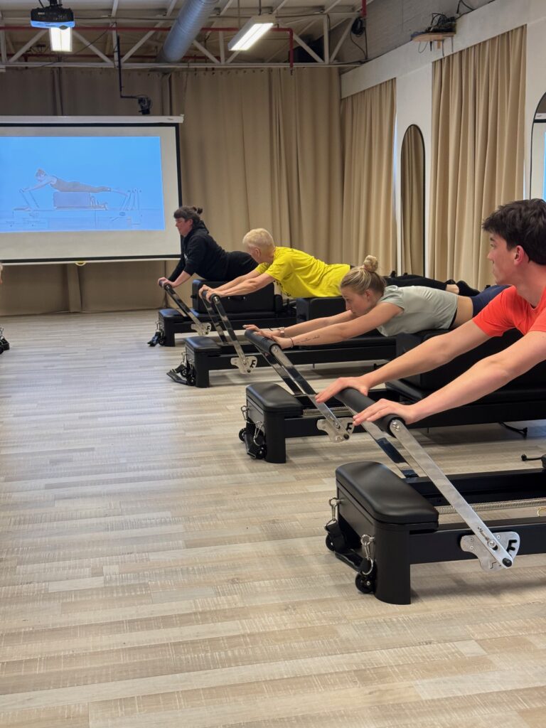 Groep deelnemers voert samen een long stretch uit op de Reformers bij Fitality Deurne