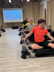 Man voert zittend een armoefening uit op de Reformer tijdens een pilatesles bij Fitality Deurne