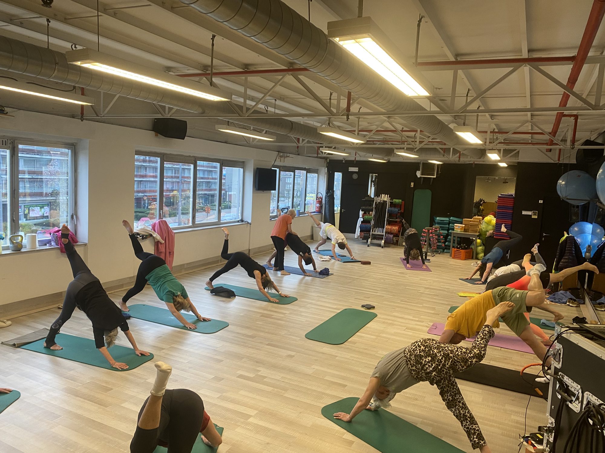 Groep leden doet een mobiliteitsoefening op matten in de grote groepszaal van Fitality Deurne