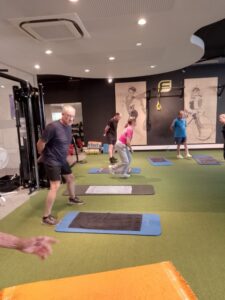 Leden doen een oefening naast hun mat tijdens een groepstraining op het kunstgras van Fitality Merelbeke
